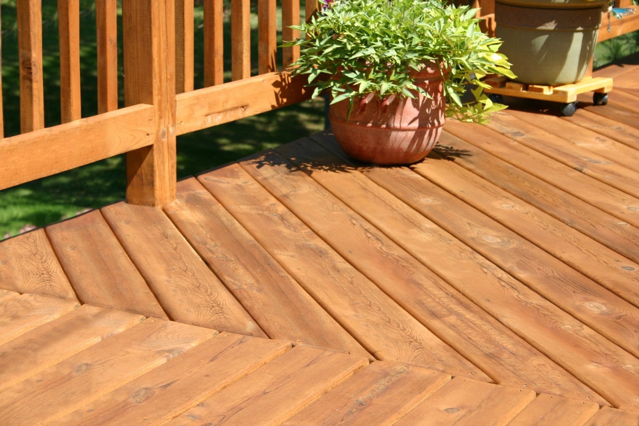 A wooden deck with a potted plant placed in the corner, next to a wooden railing.