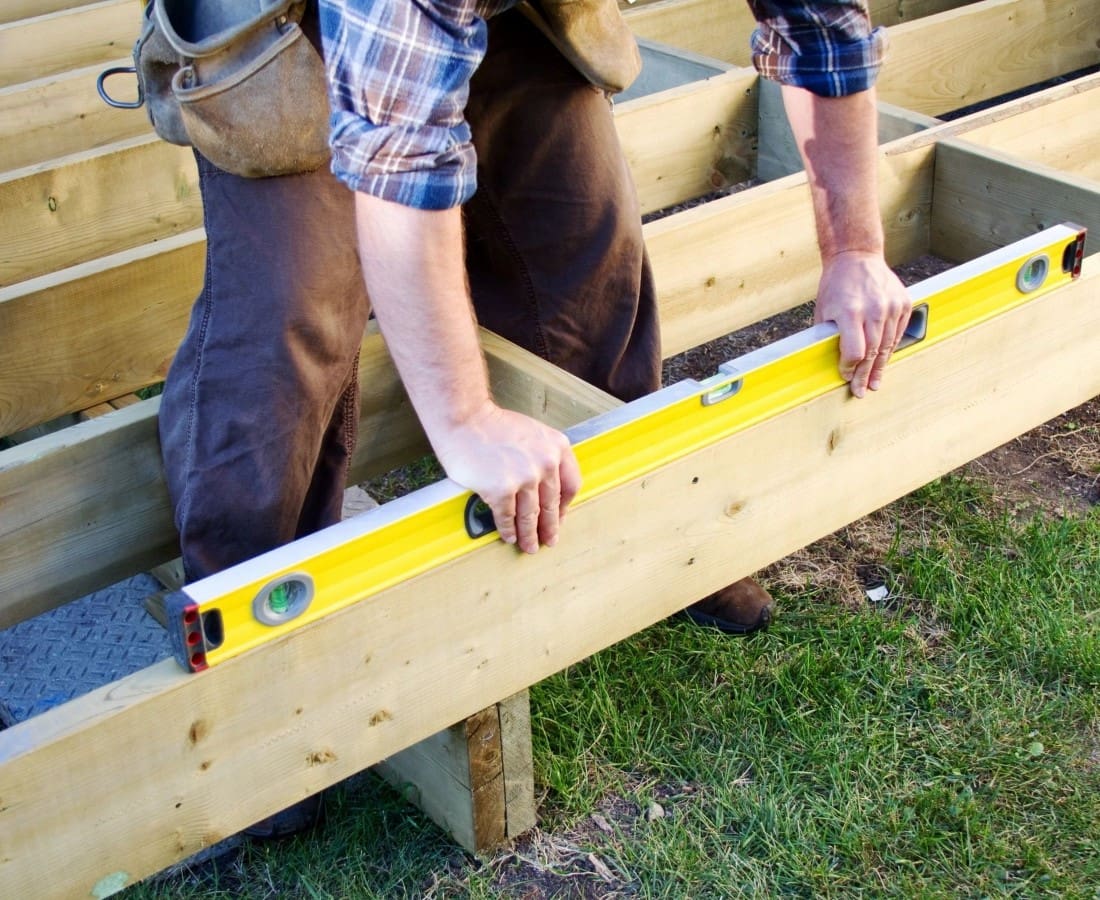 A person using a yellow spirit level to check the alignment of wooden beams in a construction project.