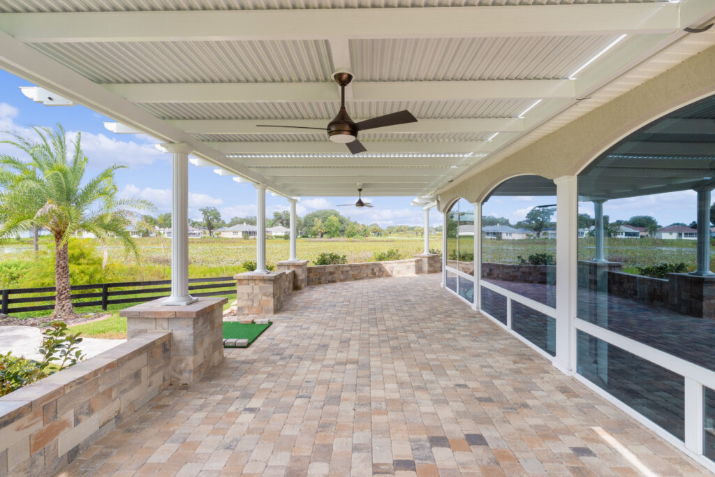 Louvered pergola providing shade over a spacious outdoor patio with stone walls, ceiling fan, and views of green landscaping, illustrating quality craftsmanship in outdoor living solutions.